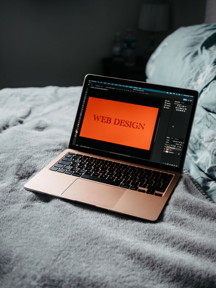 home-img A laptop on a bed showing web design software, creating a cozy workspace.